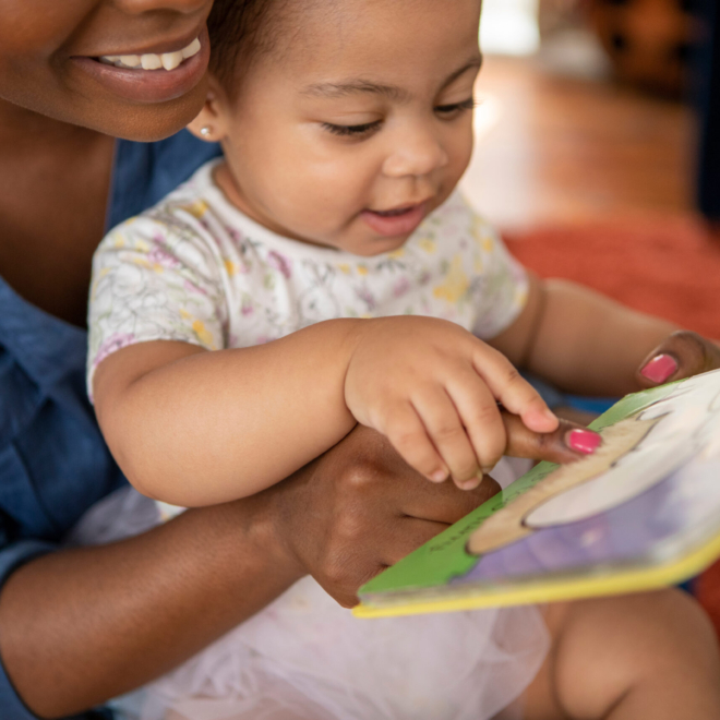 Mother Reading To Baby Daughter At Home